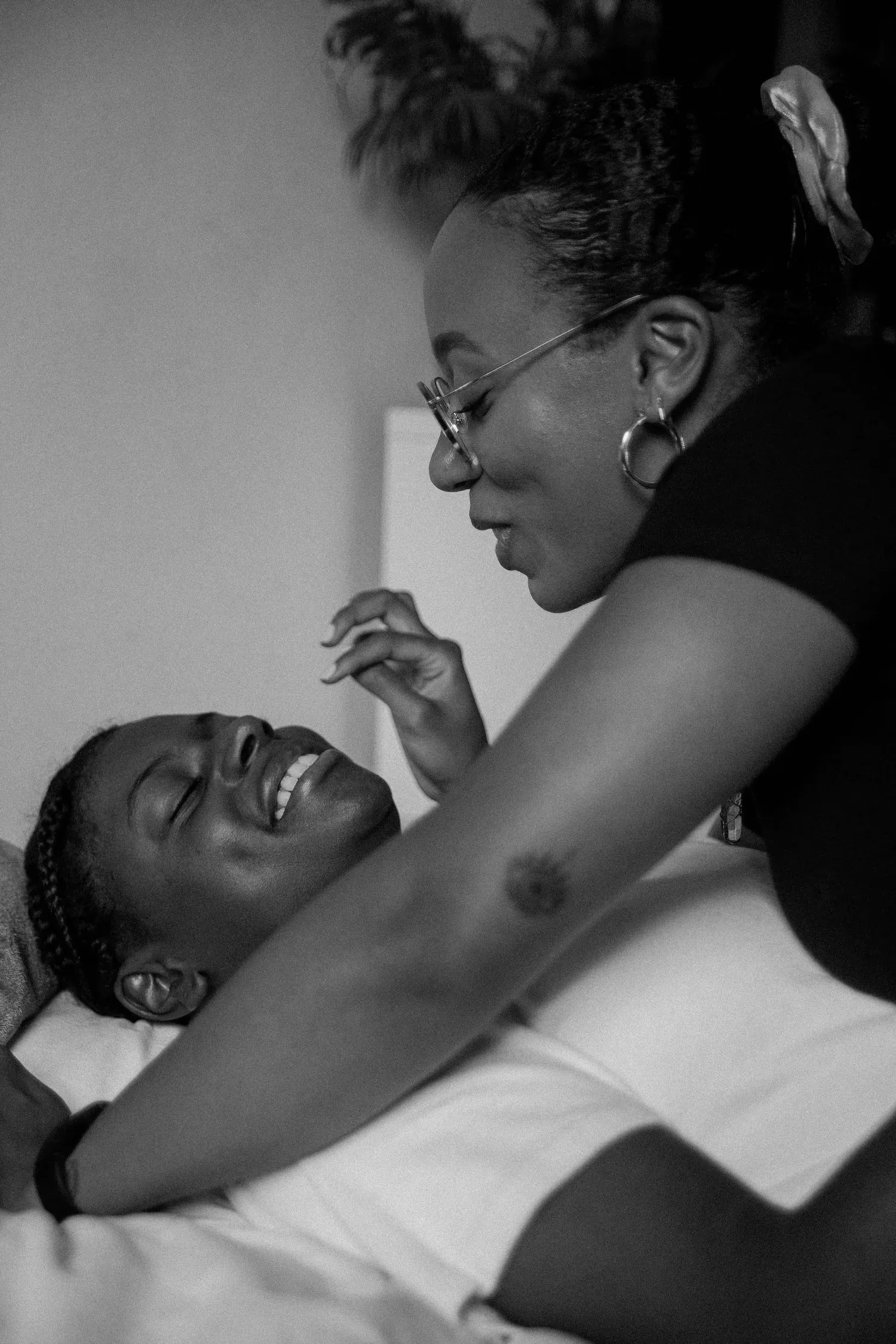 Black-and-white photo of two women laughing, one lying back in the other’s arms