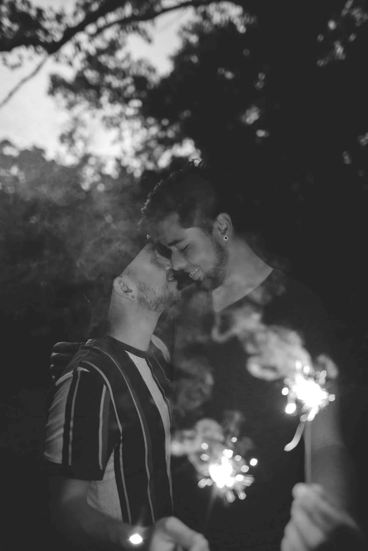Black-and-white photo of a couple embracing while holding sparklers at night