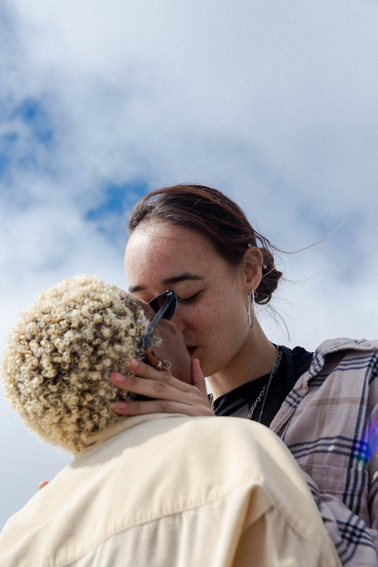 Two women kissing outdoors under a blue sky