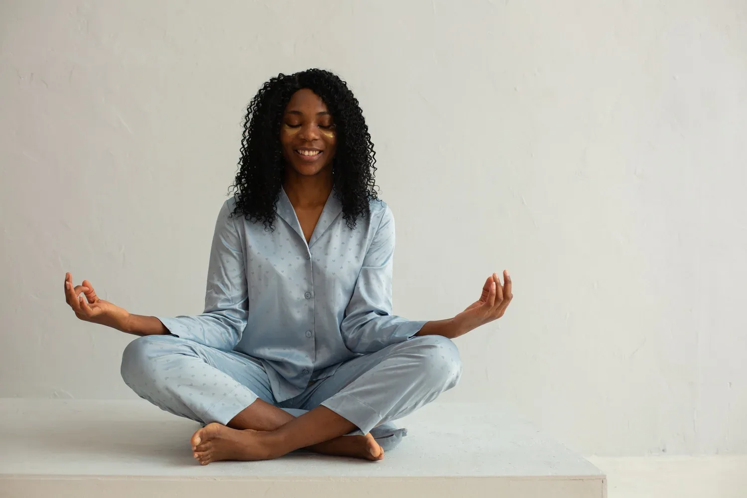 Smiling woman meditating cross-legged on the floor against a white wall