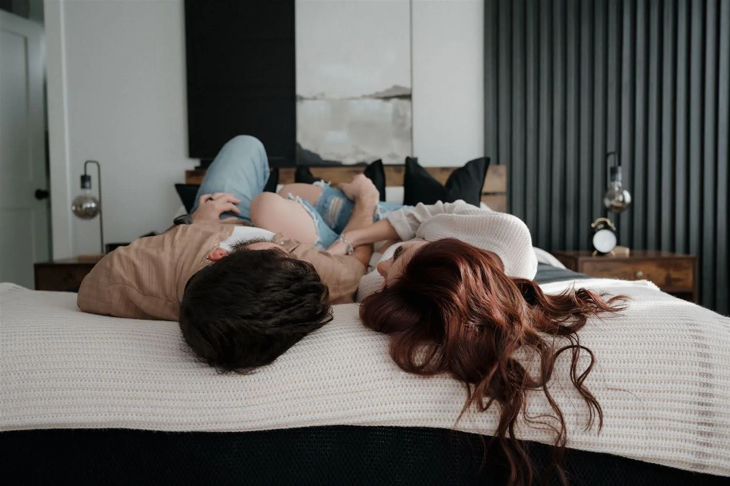 Two people lying on a bed with their heads close together, talking quietly