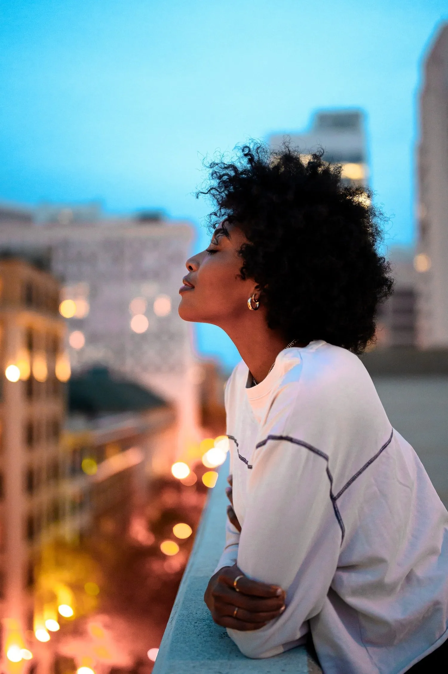 Person with curly hair looking out over a city at twilight