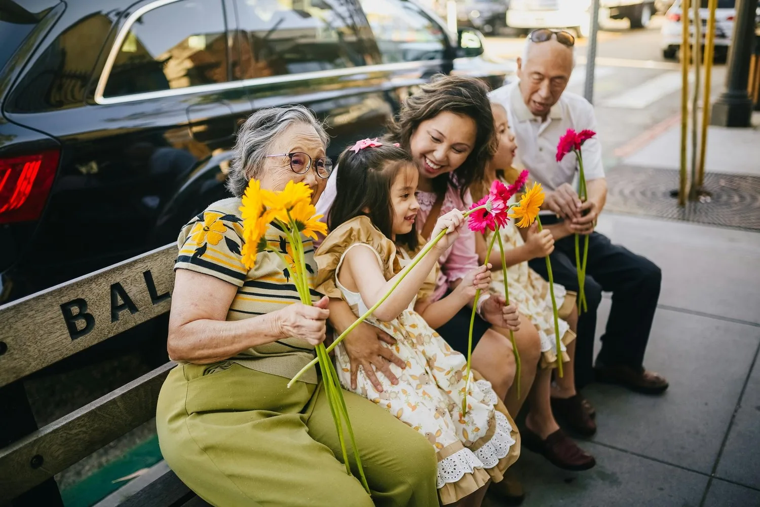 Multigenerational family holding flowers and smiling together on a sidewalk