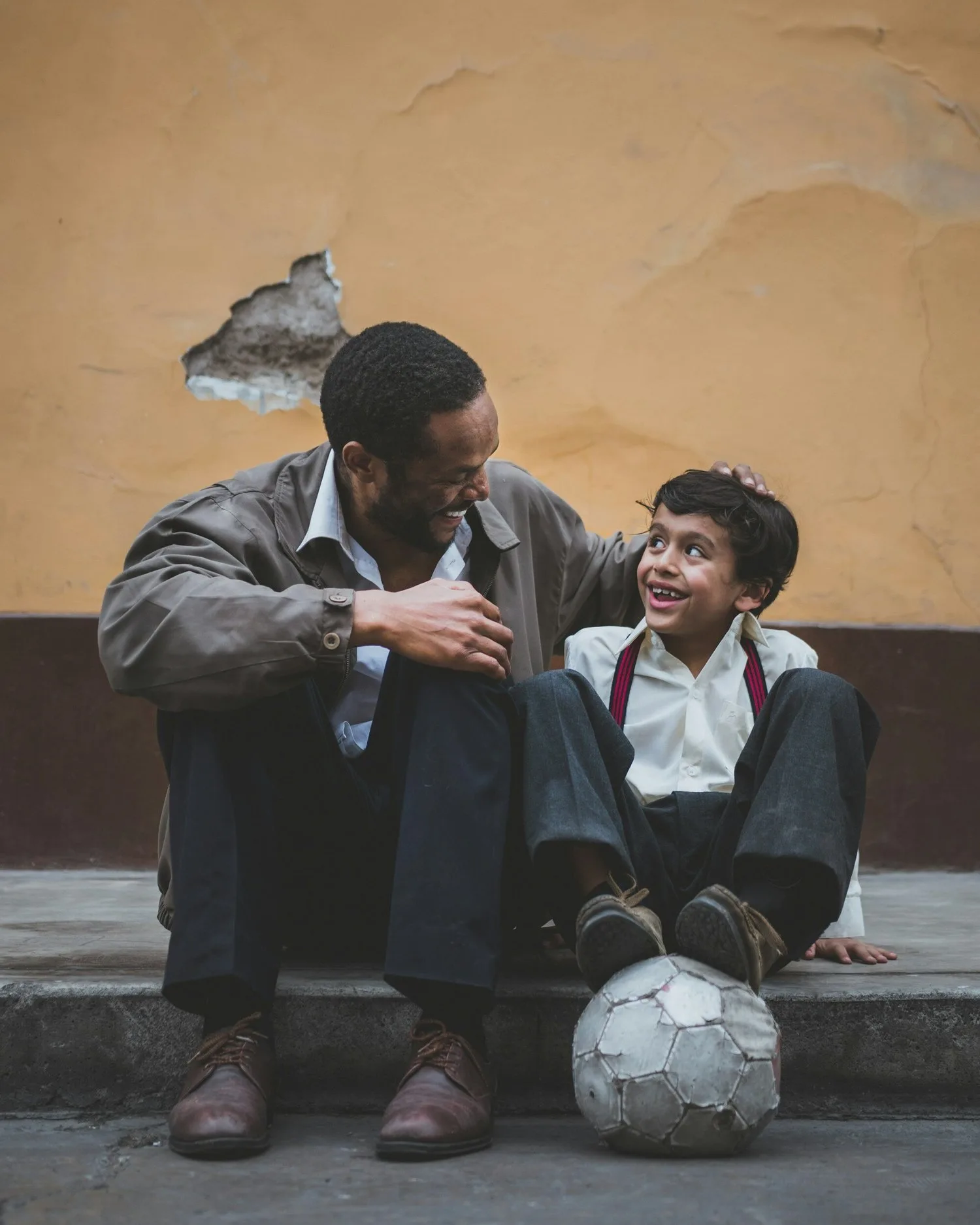 Father and son sitting together on a curb with a soccer ball