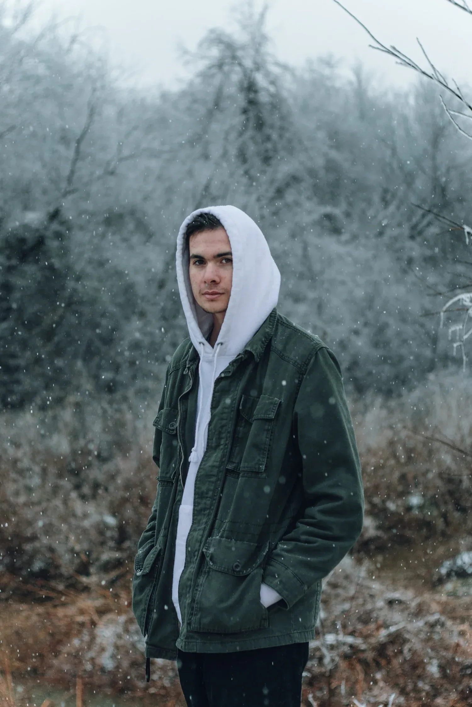 Young man in a white hoodie standing in a frosty forest
