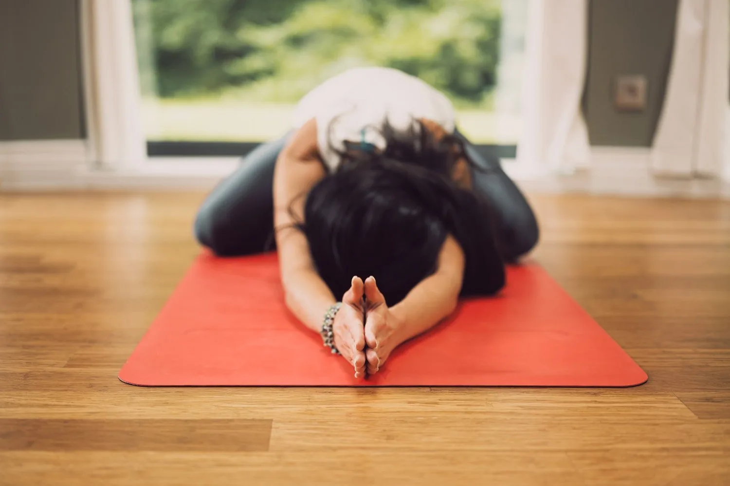 Person resting in a child’s pose on an orange mat by a window