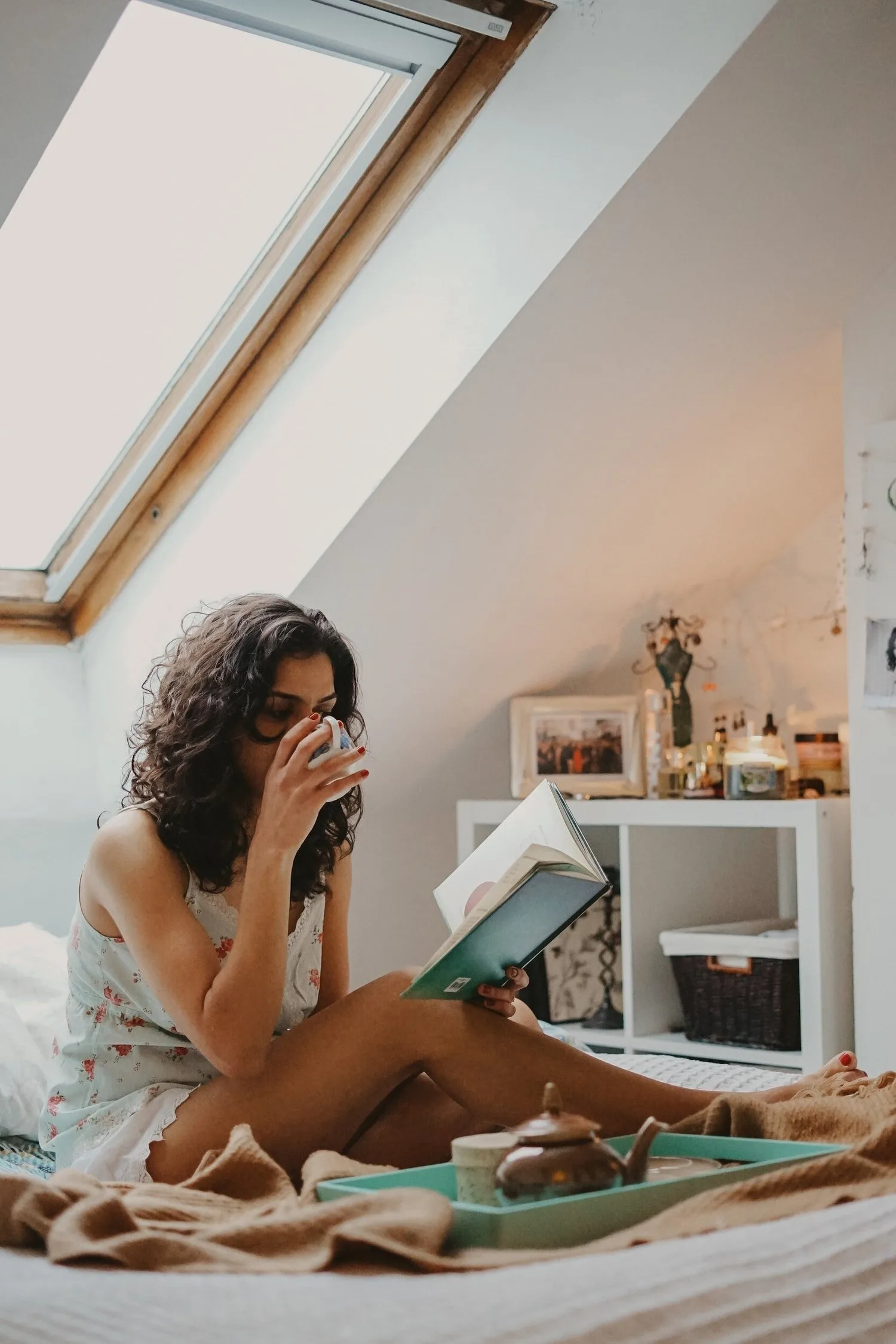 Woman sitting on the floor of an attic room reading and sipping tea
