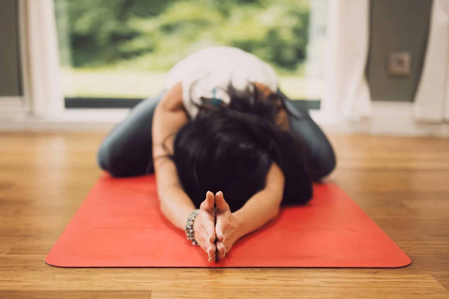 Person resting in a child’s pose on an orange mat by a window