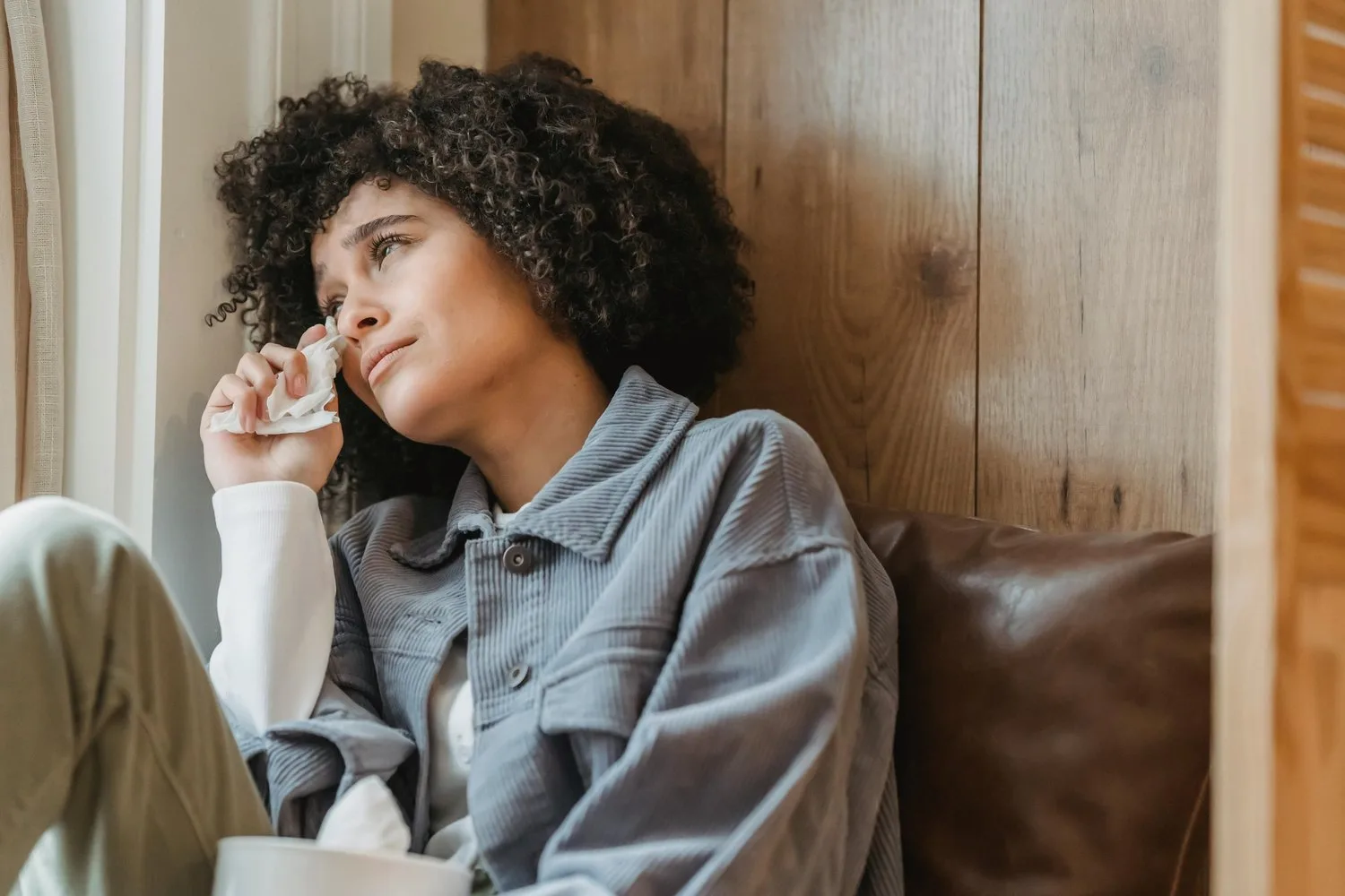 Tired young woman in a denim jacket leaning back and rubbing her eye