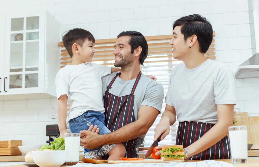 Two fathers and their young son cooking together in a bright kitchen