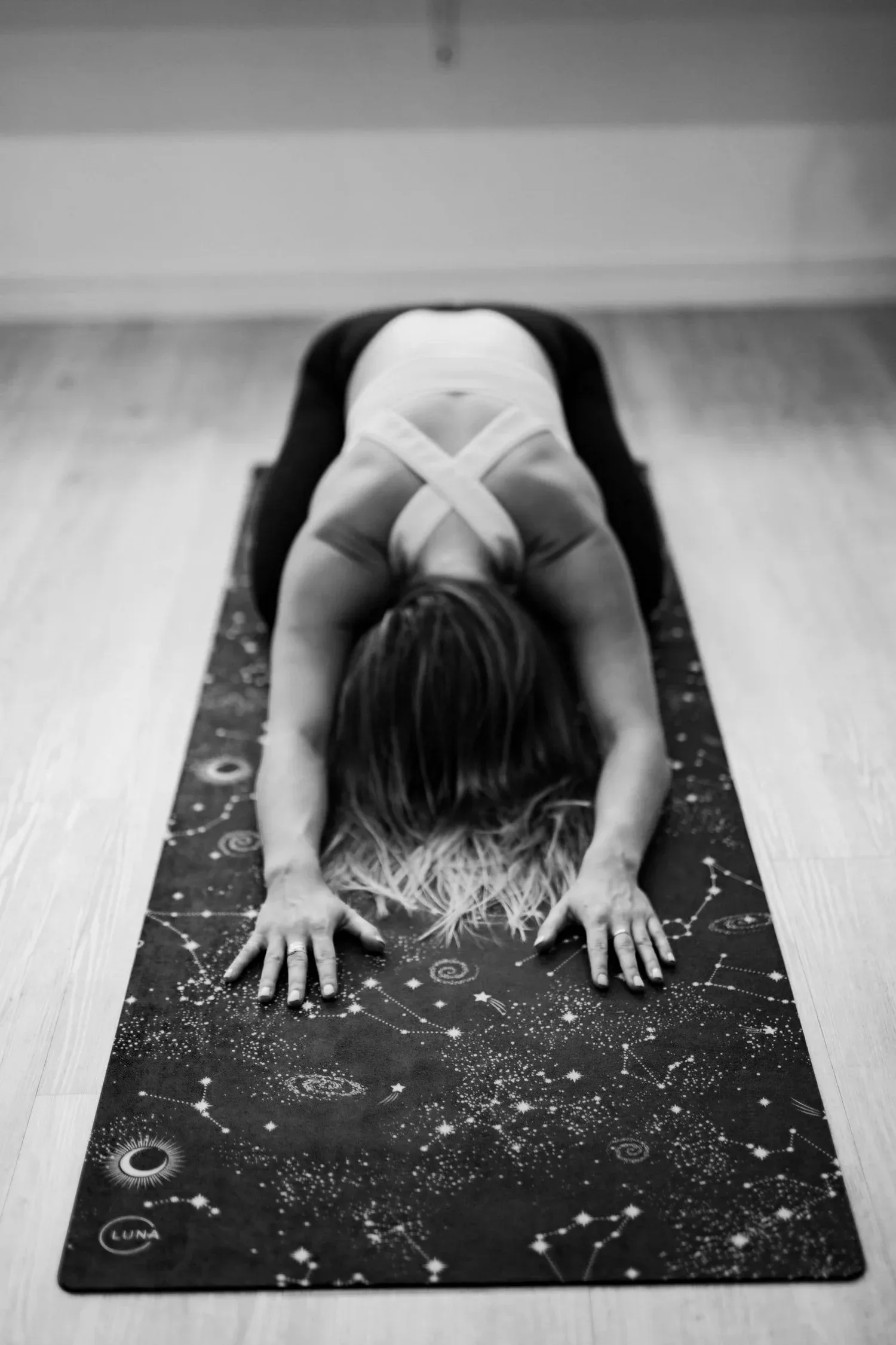 Black-and-white photo of a person in a forward fold on a patterned mat