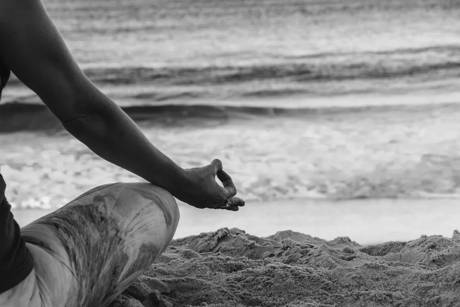 Person seated on a beach reaching toward the sand