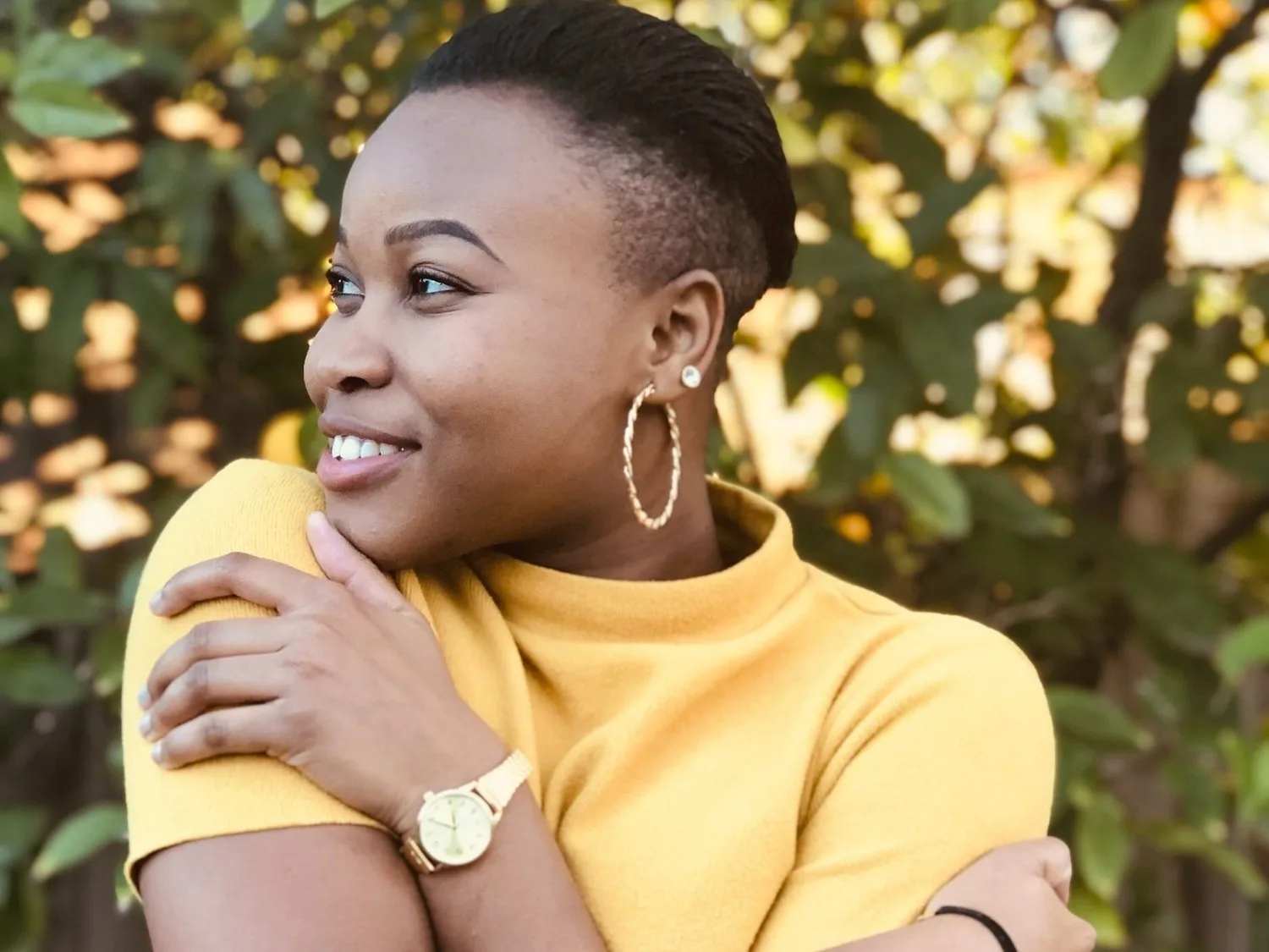 Smiling woman in a yellow top with large hoop earrings, seated outdoors