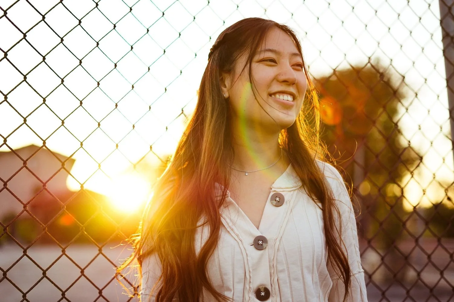 Smiling young woman in golden sunlight beside a chain-link fence