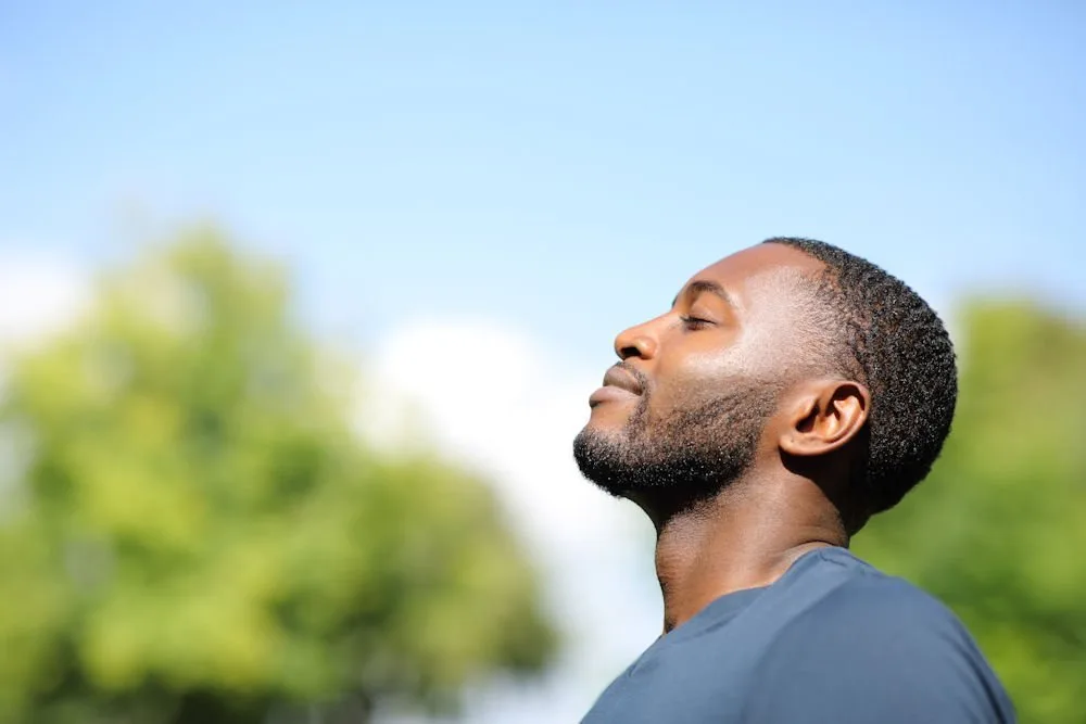Man with eyes closed tilting his face toward the sun outdoors