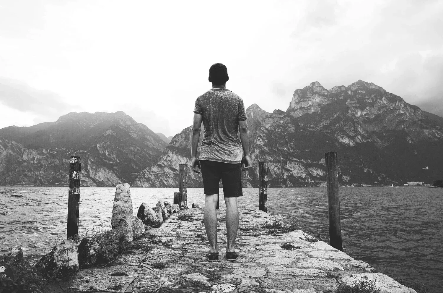 Black-and-white photo of a person standing on a rocky ridge facing mountains