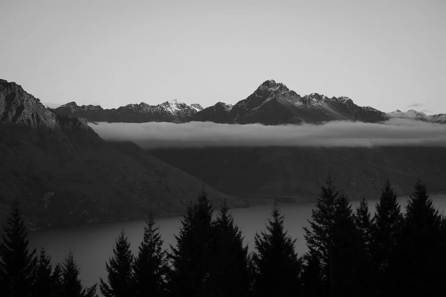 Black-and-white photo of a mountain lake with a dark tree line