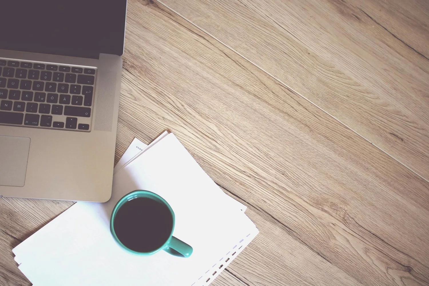 Laptop, notebook, and coffee cup on a wooden desk seen from above