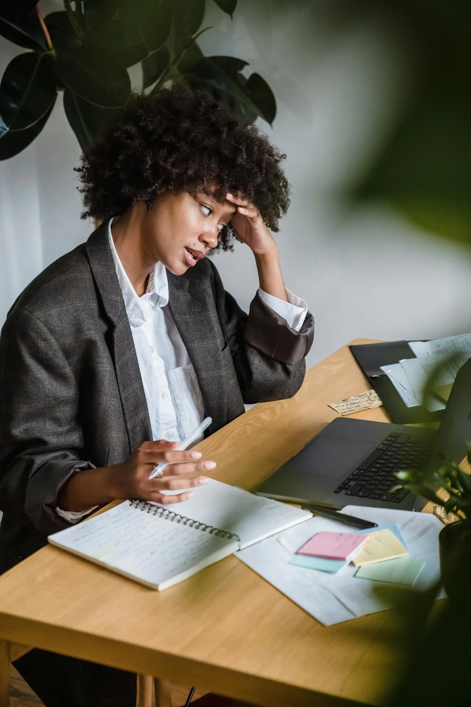 Woman at a desk with a laptop and notebook, hand pressed to her forehead in frustration