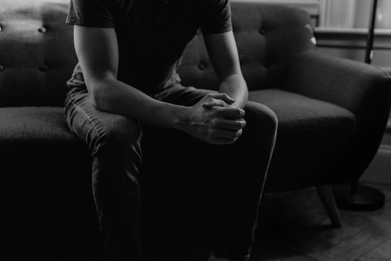 Black-and-white photo of a person seated with hands clasped between their knees