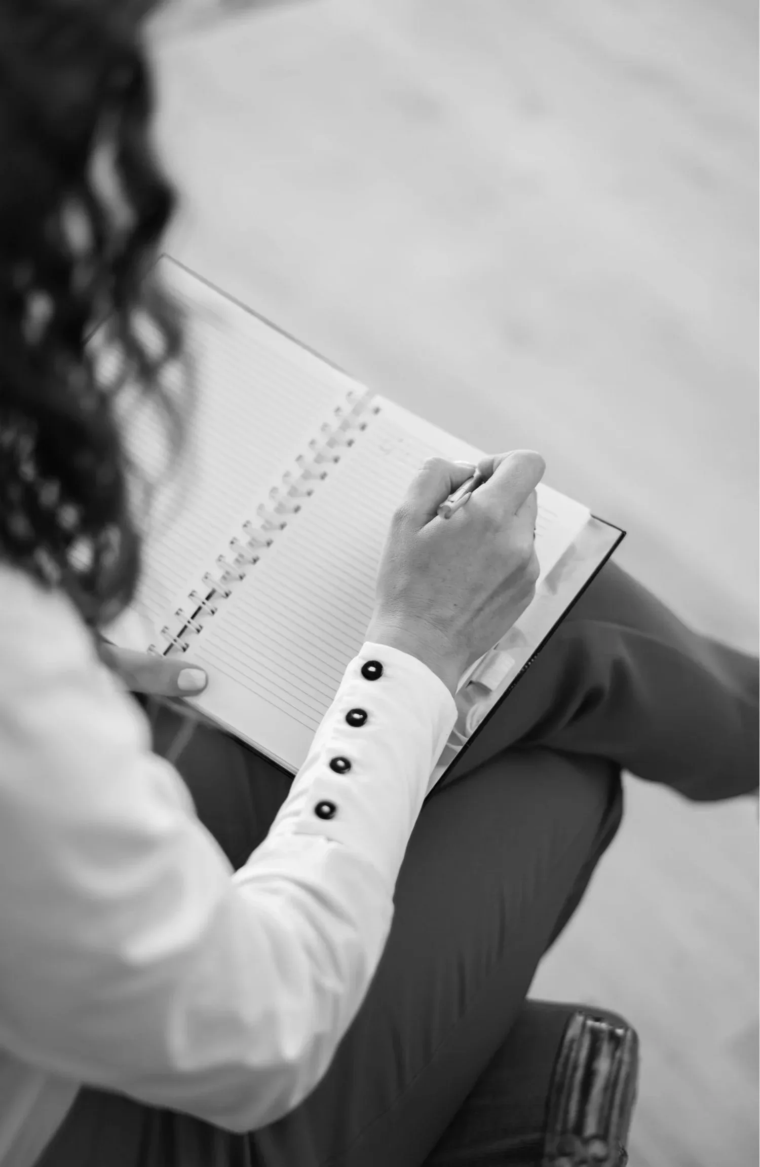 Black-and-white photo of a person writing on a notepad in their lap