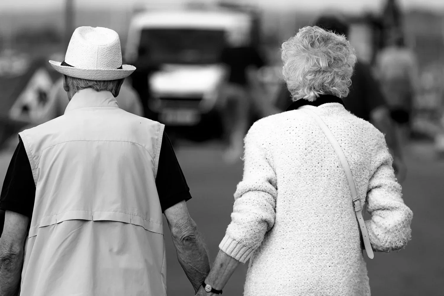 Black-and-white photo of an older couple walking arm in arm down a street