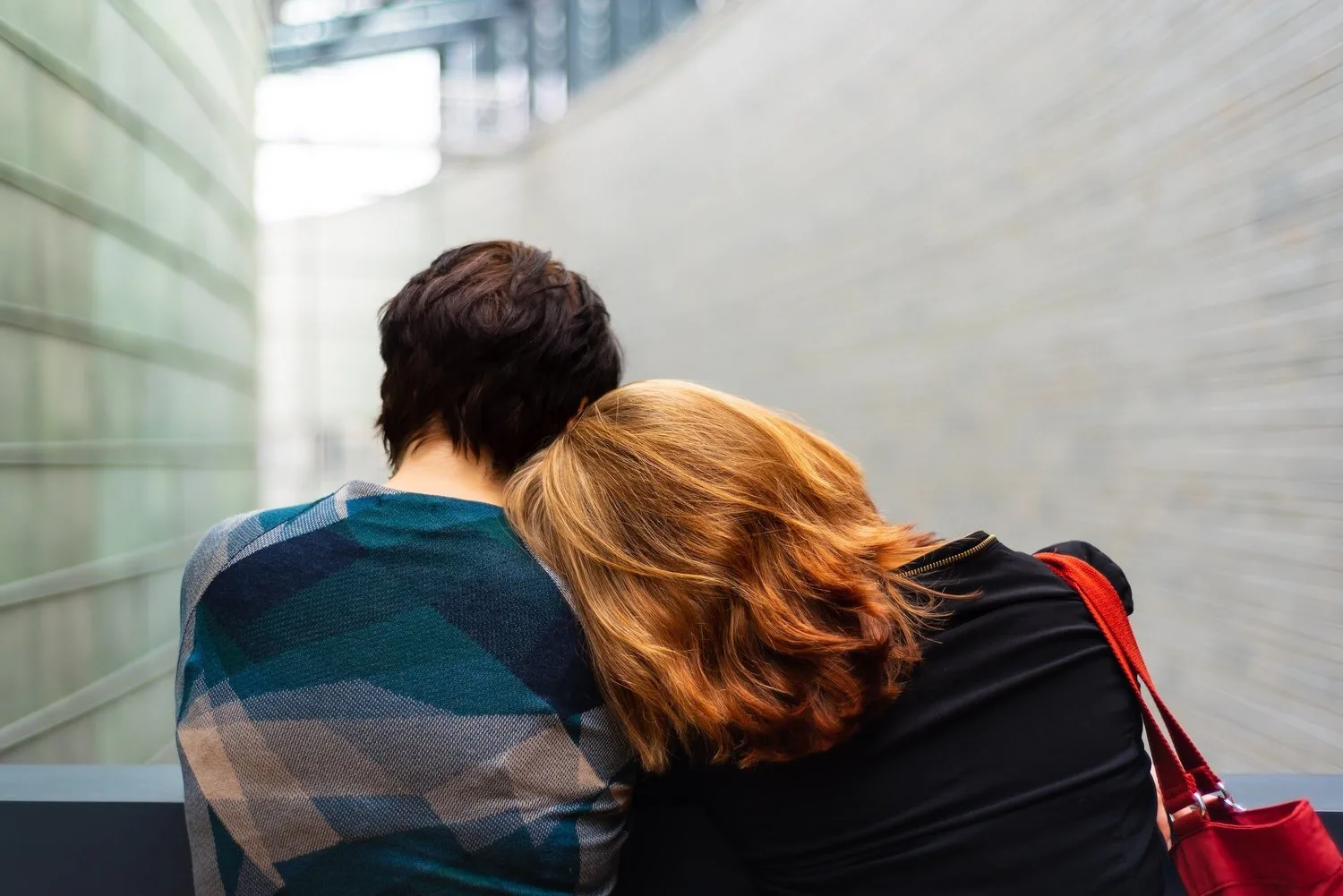 Two people sitting close together, one resting a head on the other’s shoulder