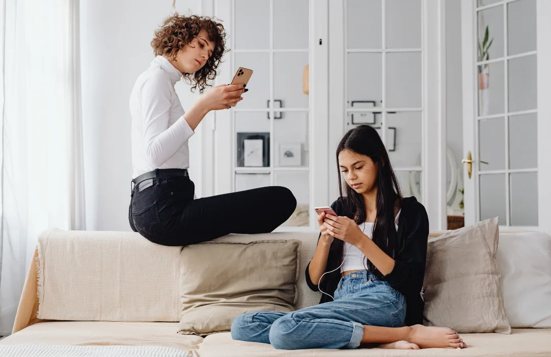 Parent and teen sitting apart on a sofa, both looking at their phones