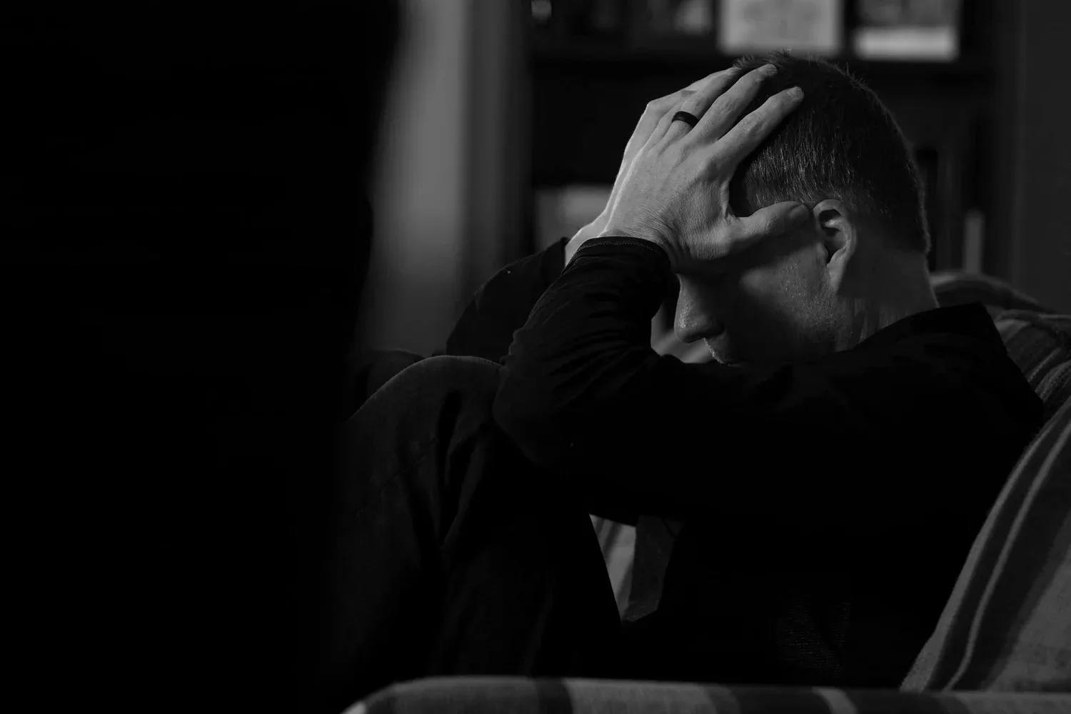 Black-and-white photo of a man holding his head in his hand in shadow