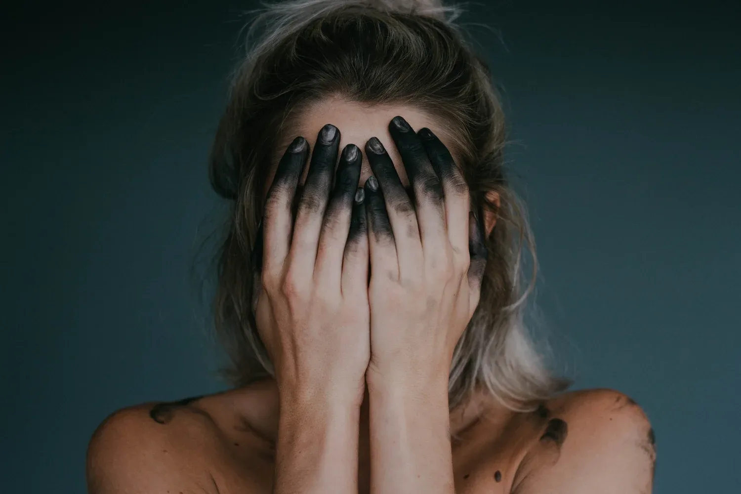 Woman covering her face with both hands, fingernails painted dark