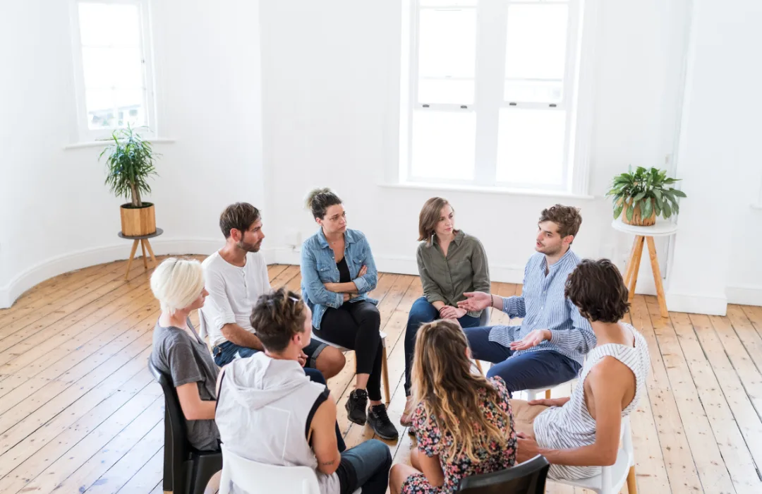 Group of adults seated in a circle in a bright room for a group discussion