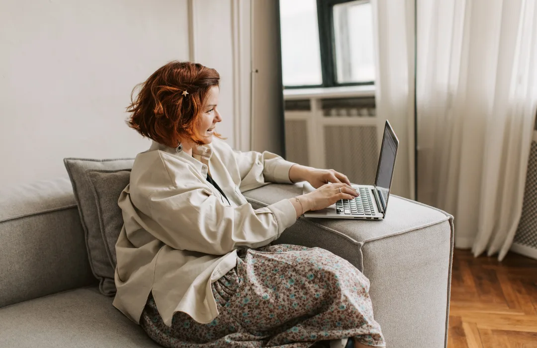 Woman working on a laptop on a sofa in a bright living room