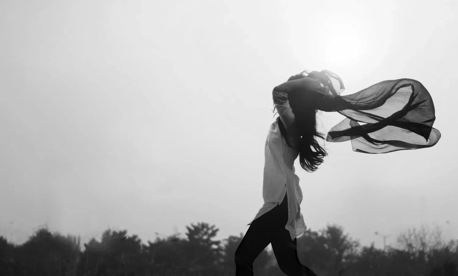 Black-and-white photo of a person walking in a field with fabric blowing in the wind