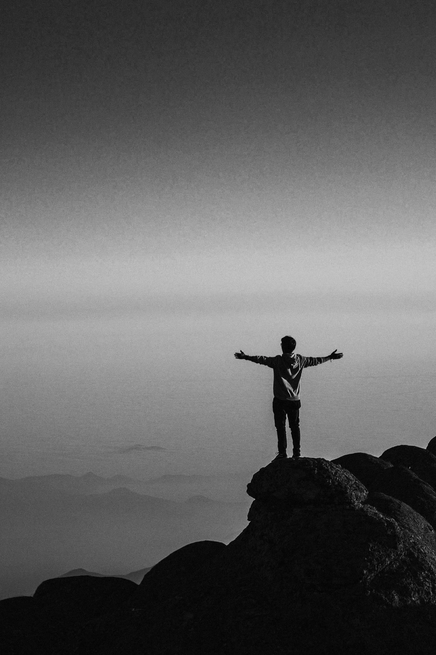 Silhouette of a person with arms outstretched on a rock at dusk