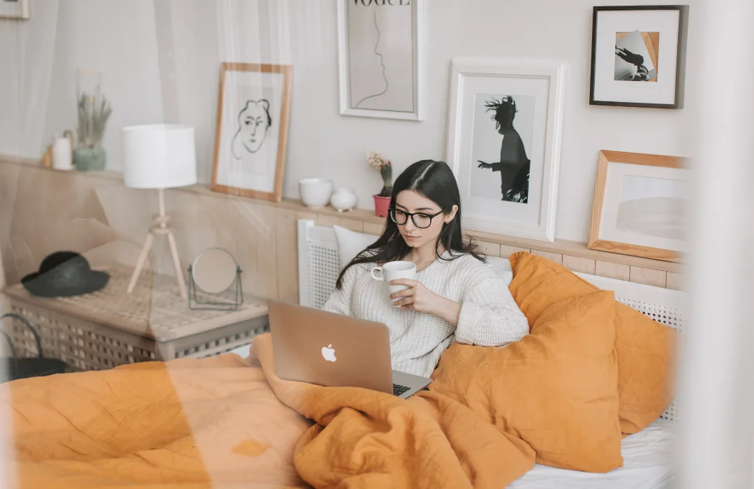 Woman working on a laptop in a cozy living room with an orange blanket