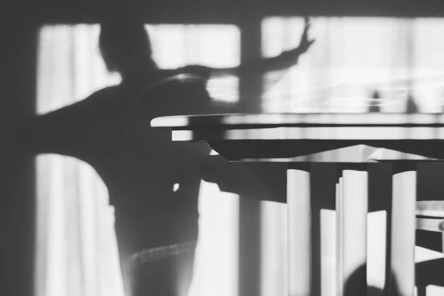 Black-and-white photo of a hand casting a shadow across window blinds