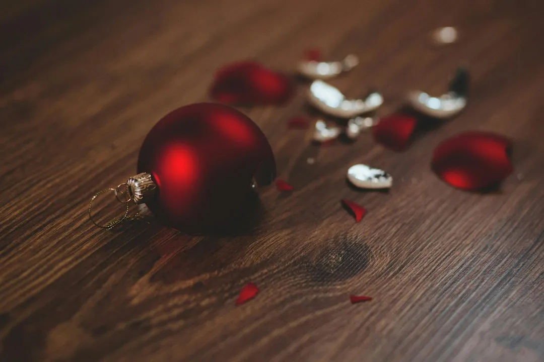 Broken red holiday ornament scattered on a wooden floor