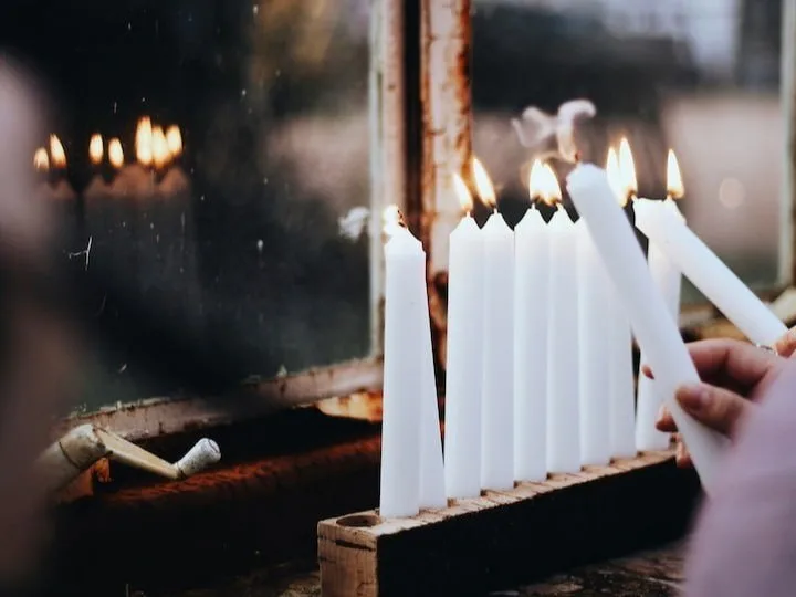 Hand lighting a row of white candles in a dim room
