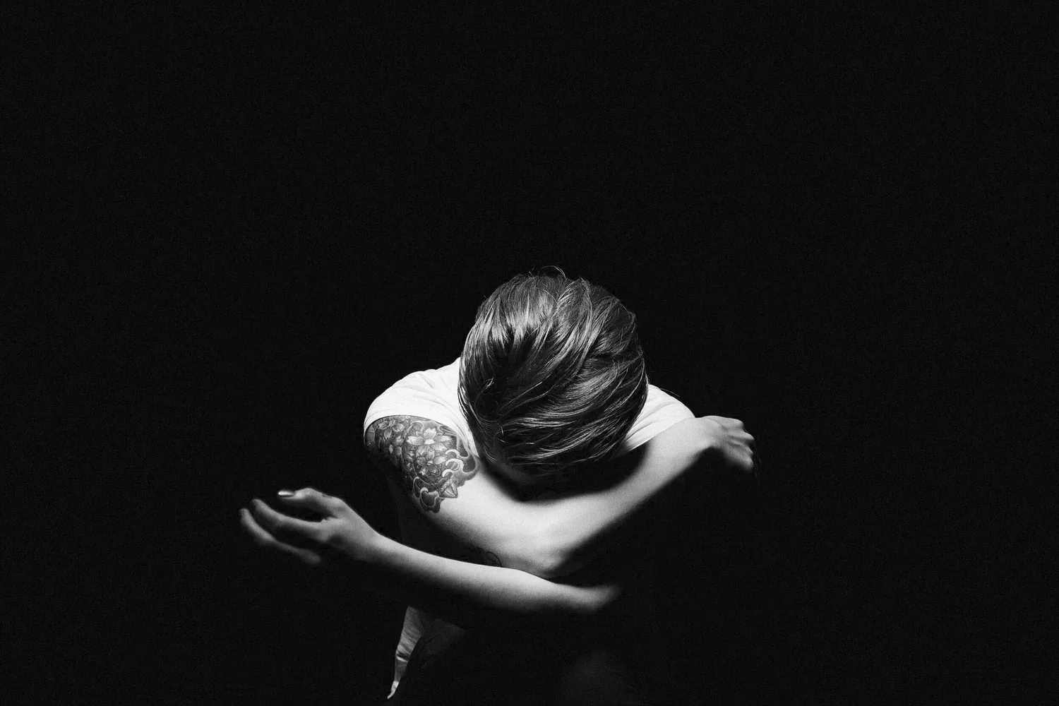 Black-and-white photo of a person hugging themselves in darkness