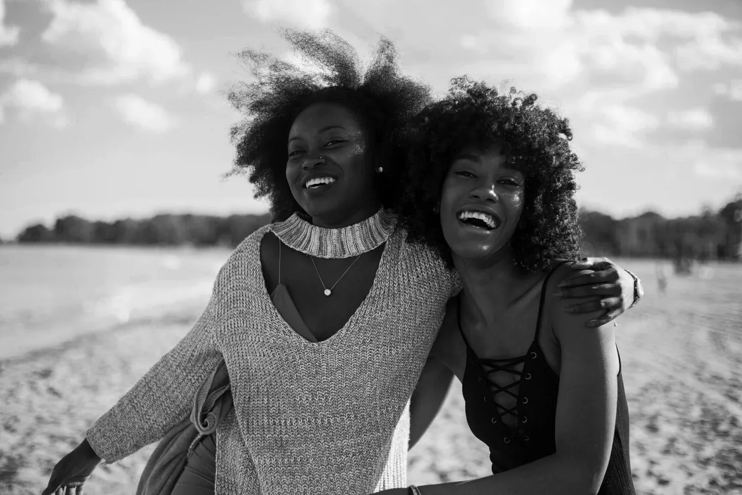 Black-and-white photo of two women laughing and embracing on a beach