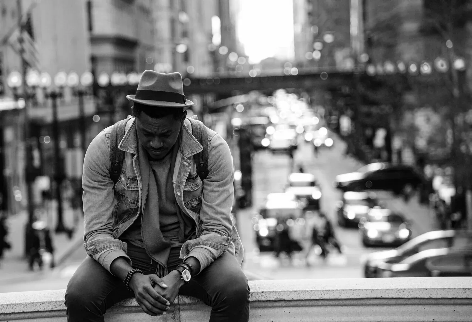 Black-and-white photo of a man in a hat sitting on a city ledge above traffic
