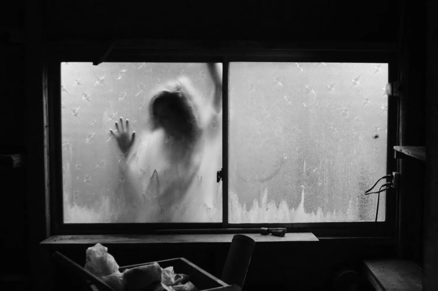Black-and-white photo of a person pressing their hands against a foggy window