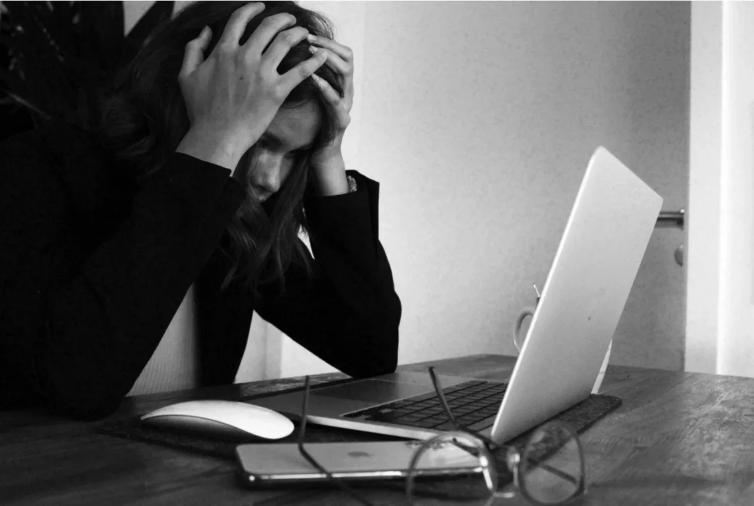 Black-and-white photo of a stressed person with head in hands at a laptop