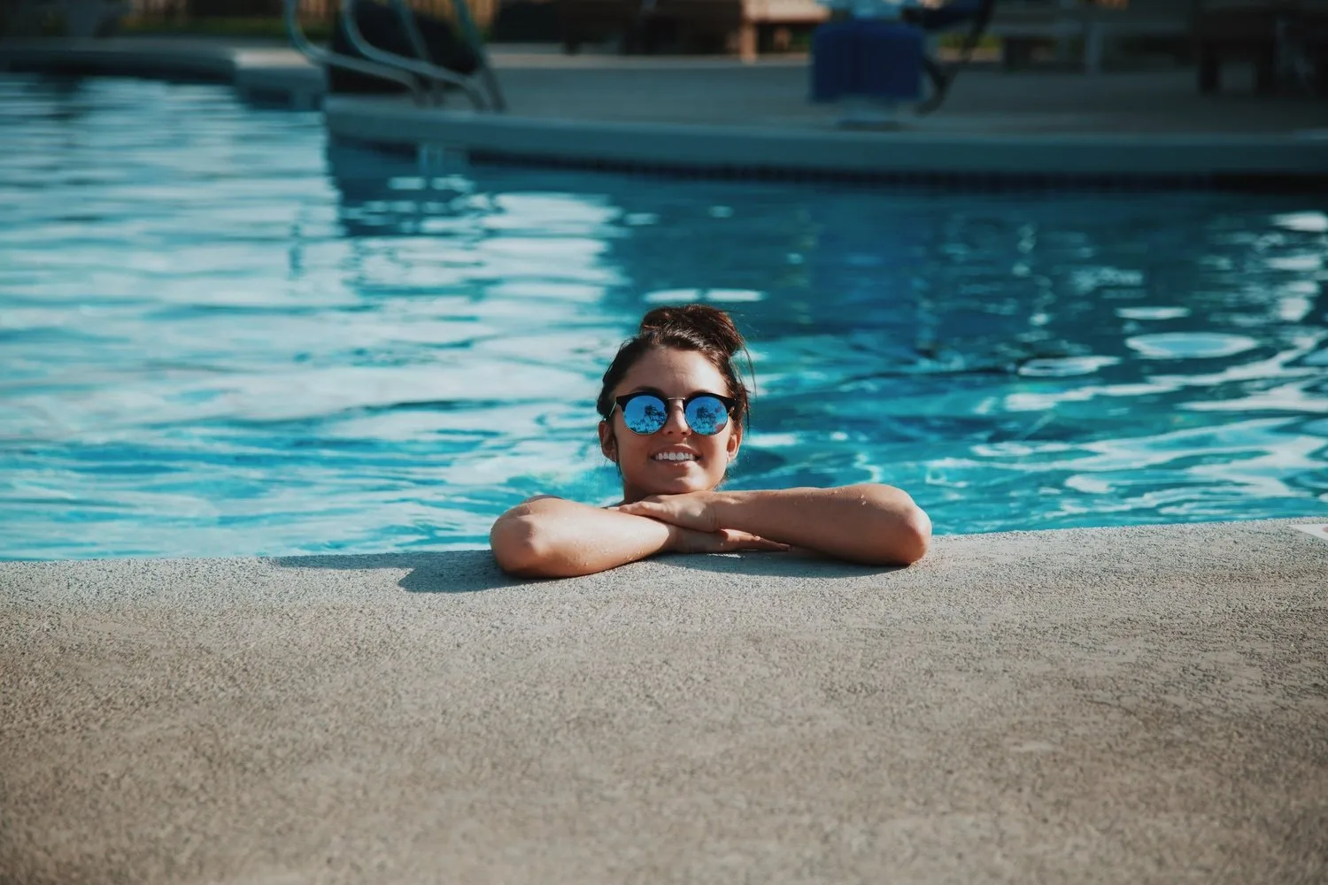 Person in sunglasses resting at the edge of a swimming pool