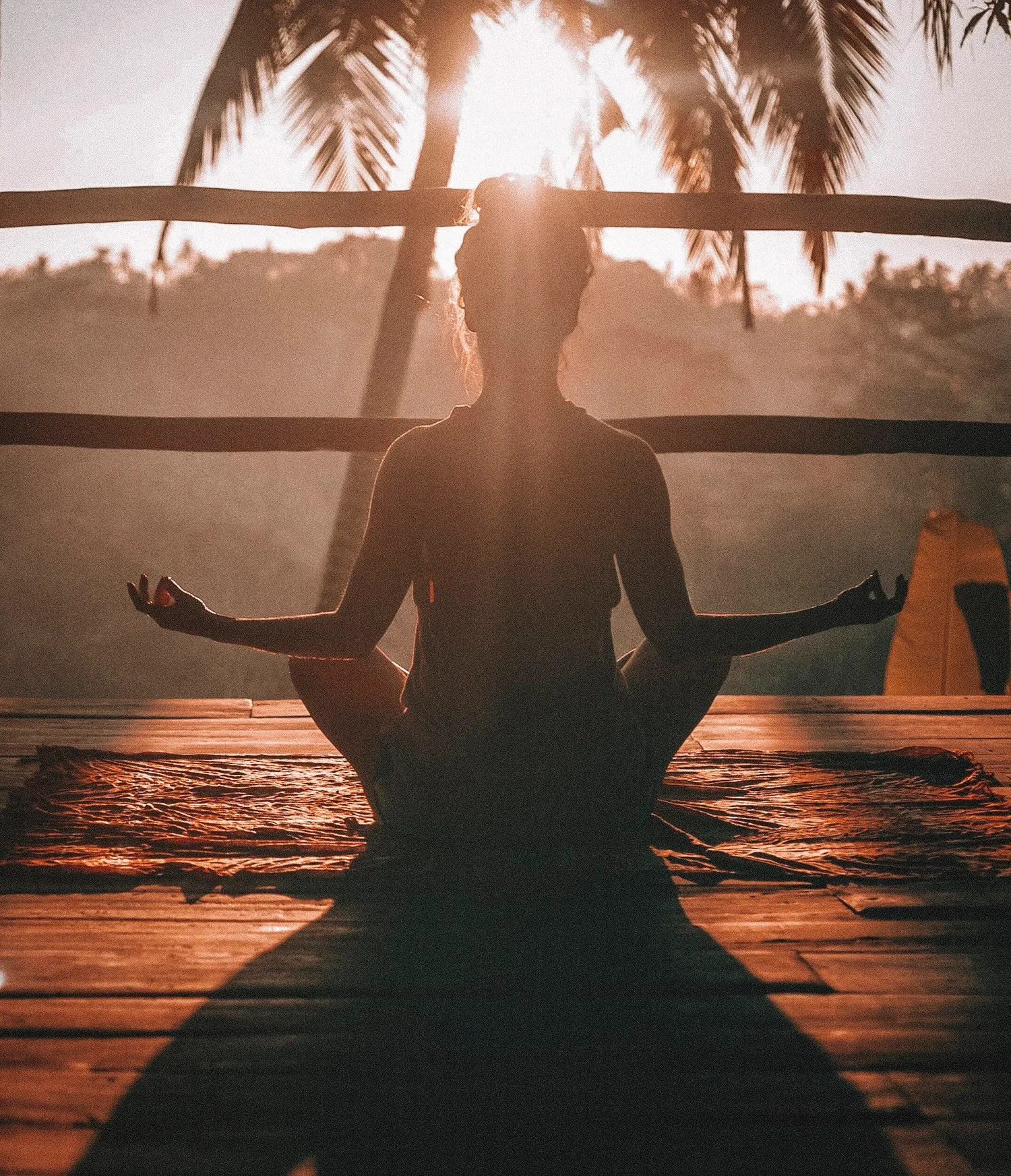 Person meditating on a wooden deck at sunset, casting a long shadow
