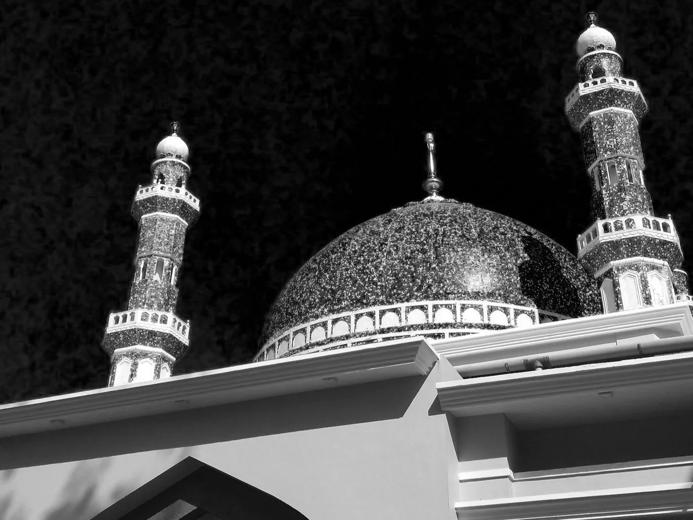 Black-and-white photo of a mosque dome and minarets at night