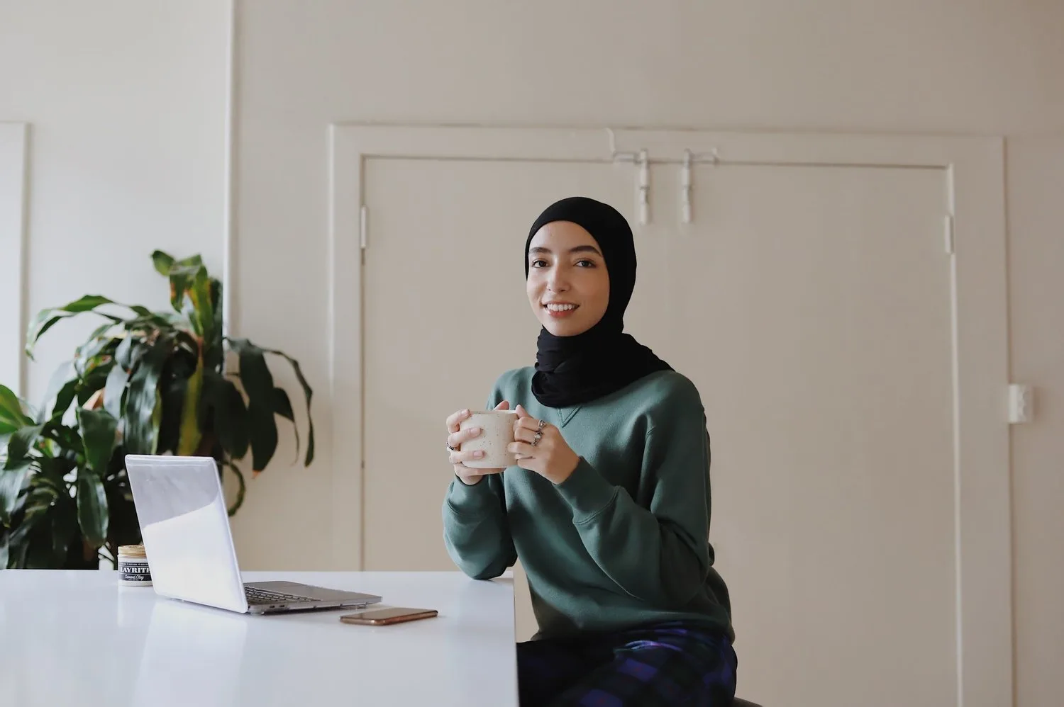 Woman in a hijab speaking and gesturing at a desk in a bright office