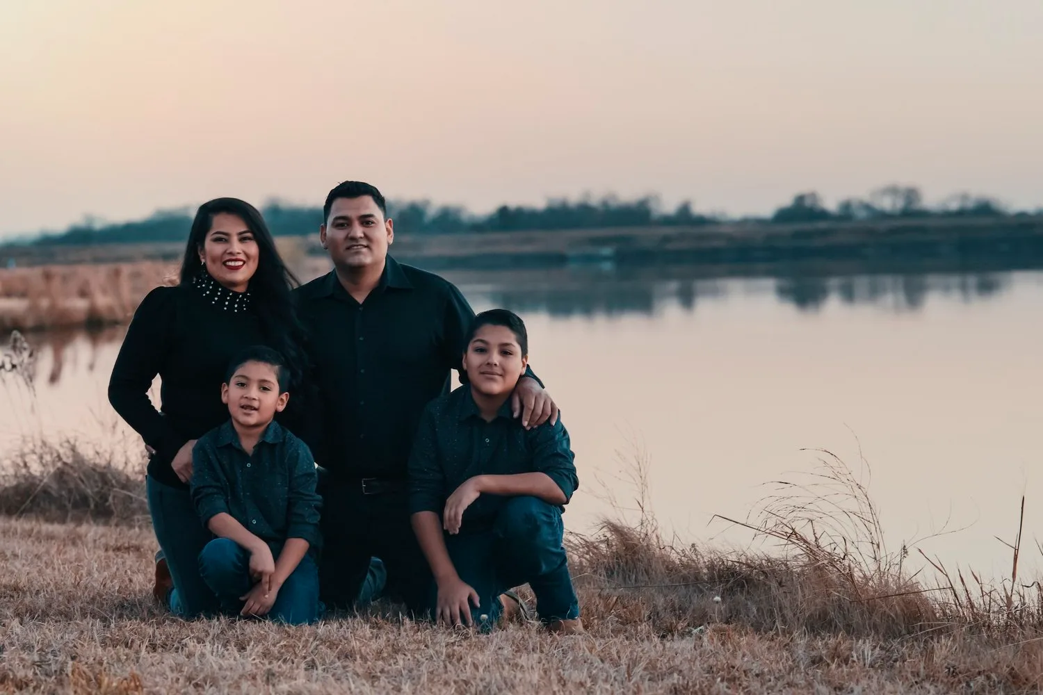 Family of four posing together by a lake at sunset