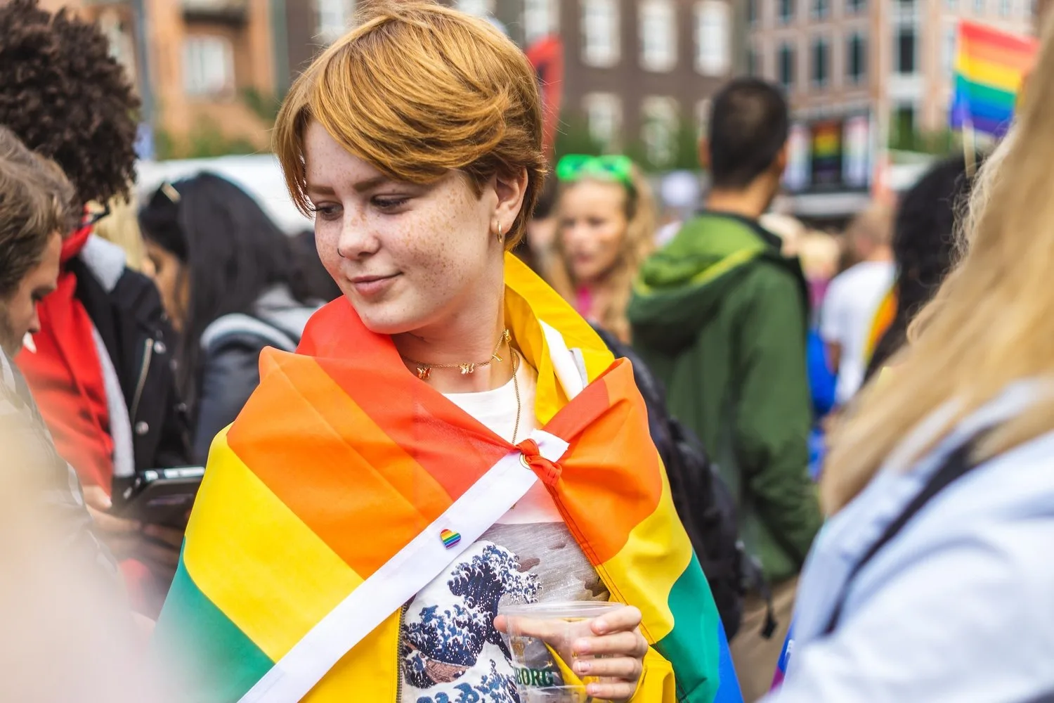 Young person wrapped in a rainbow Pride flag at a city march