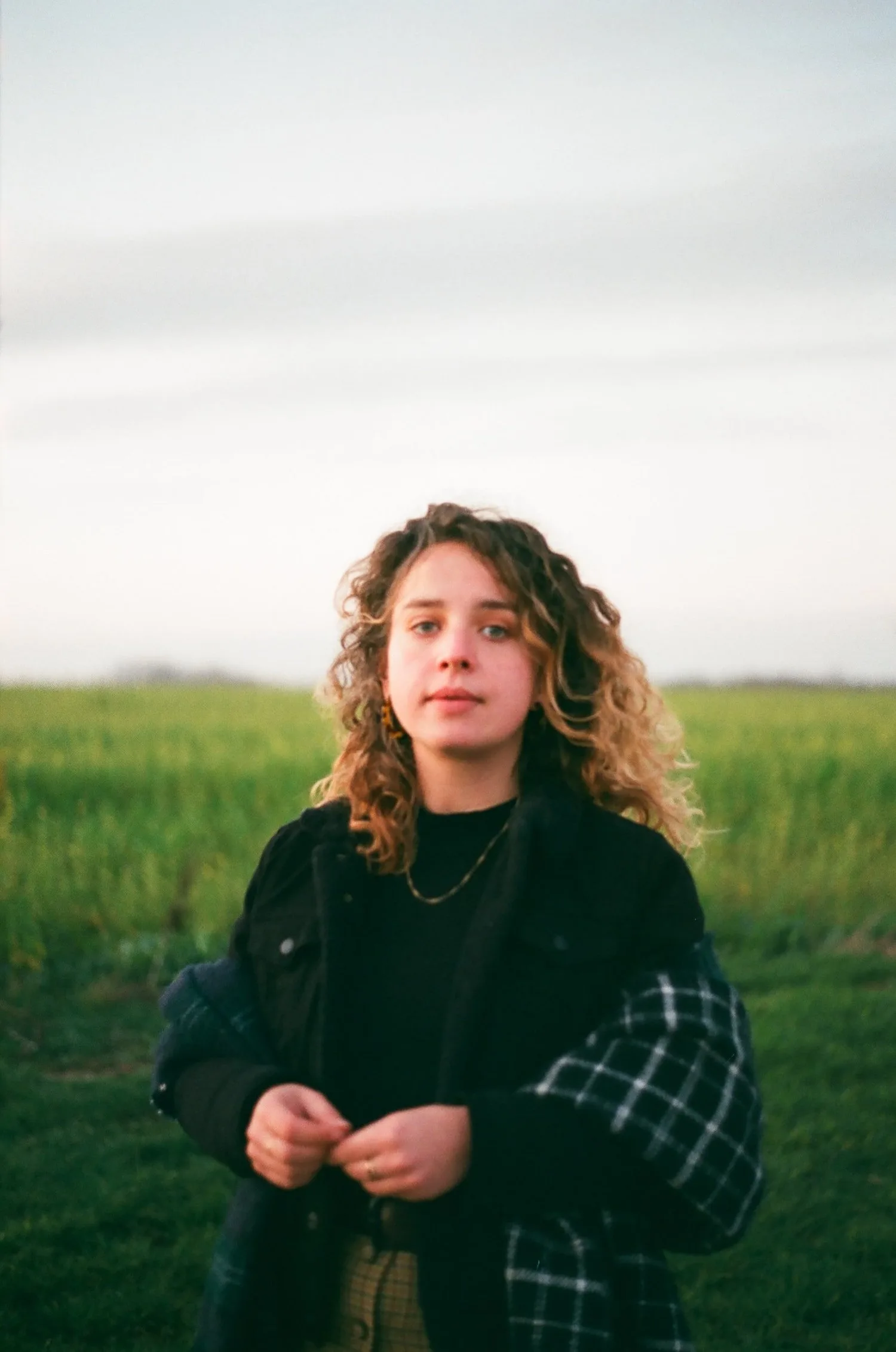 Young person with curly hair standing in a green field, looking at the camera